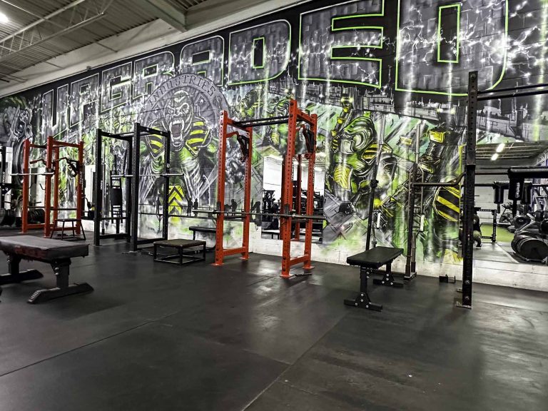 Red squat racks along the graffiti mural on the strength floor at Upgraded Industries, a 24/7 gym in Mentor, Ohio