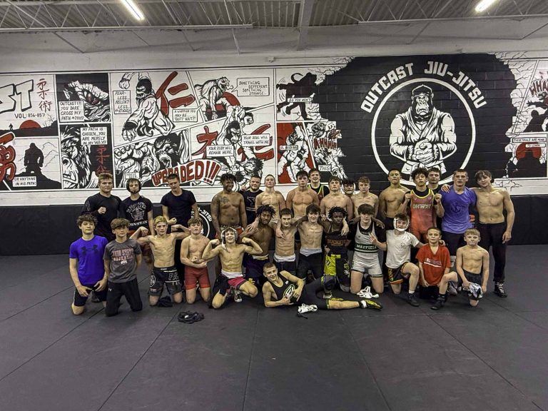 Kids and adults from the martial arts classes at Upgraded Industries posing in front of the gym mural
