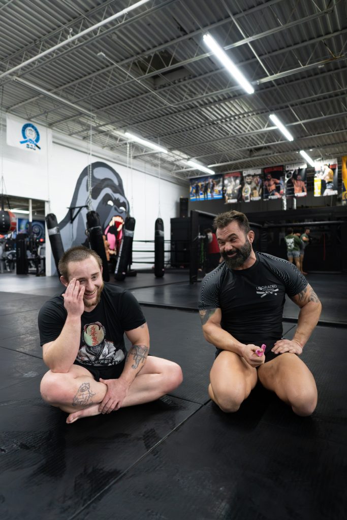 Coach and athlete talking on the mats beside the MMA cage at Upgraded Industries, a gym in Mentor, Ohio