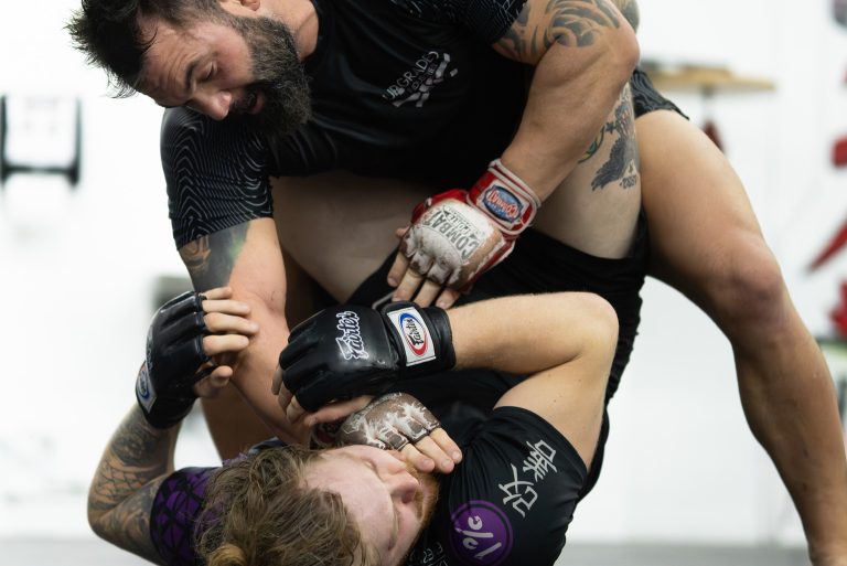 Coach controlling a training partner on the mat during an MMA grappling drill